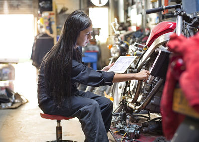 Side view of woman holding digital tablet while repairing bike in workshop