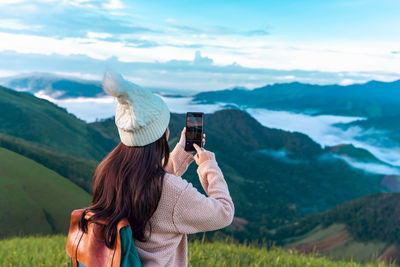 Rear view of woman photographing against sky