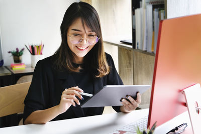 Portrait of smiling young woman using phone while sitting on table