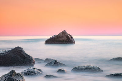 Rocks in sea against sky during sunset