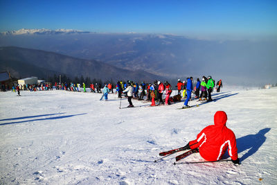 People skiing on snow covered field against mountain range