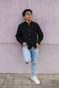 Young transgender man leaning on a wall while posing outdoors on the street.