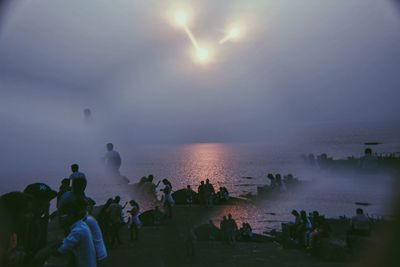 Double exposure of people at beach against sky during sunset