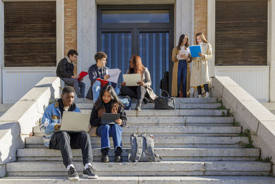 Friends studying over tablet pc and laptop on steps on campus