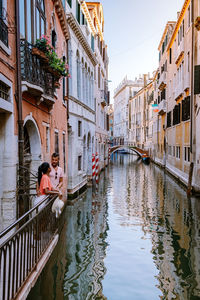 Reflection of woman on bridge over canal amidst buildings