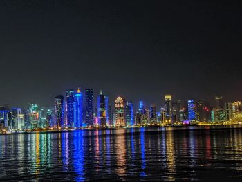 Illuminated city by river against sky at night in qatar.
