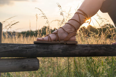 Woman with sandals relaxing on the fence at sunset.