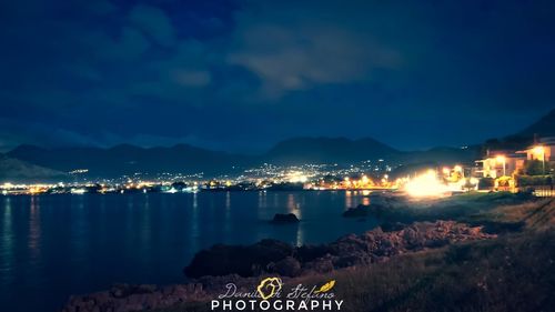 Illuminated city by sea against sky at night