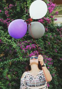 Young woman holding various balloons against flowering plant