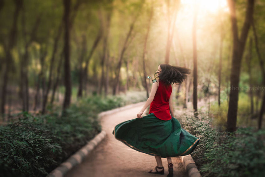 REAR VIEW OF WOMAN STANDING ON TREE TRUNK IN FOREST