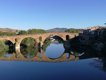 Arch bridge over river against clear blue sky