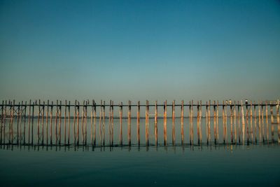 Wooden posts in sea against clear blue sky