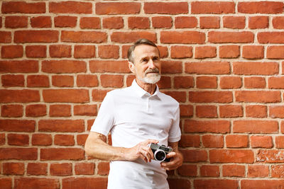 Portrait of man holding camera against wall