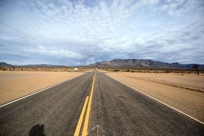 Empty road leading towards mountains against sky