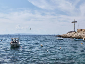 Rocky coastline of saronic gulf, aegean sea, boat and memorial cross at piraeus, attika, greece.