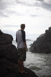 Full length of man standing on rock in sea against sky