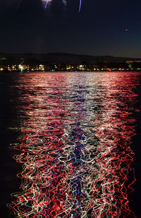 Aerial view of illuminated city by sea against sky at night