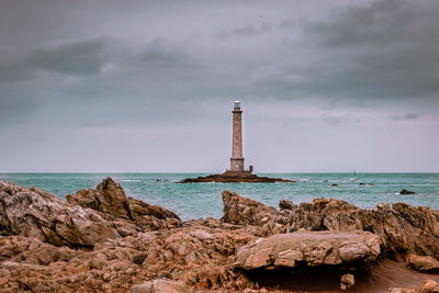 Lighthouse on rock by sea against sky