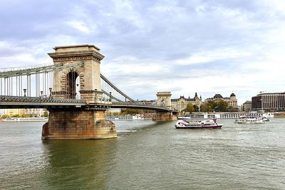 View of chain bridge over river against cloudy sky