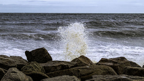 Waves splashing on rocks at shore against sky