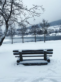 Park bench by snow covered field during winter