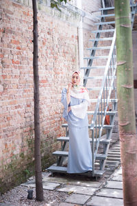 Woman standing on steps against brick wall