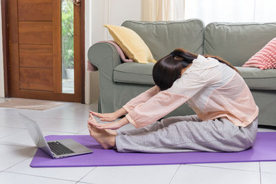 Side view of woman using laptop on bed at home