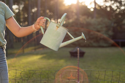 Midsection of woman holding watering can at lawn