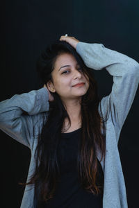 Portrait of beautiful young woman standing against black background