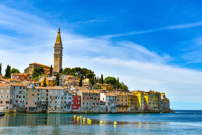 Buildings at waterfront against cloudy sky