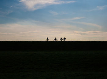 Silhouette people riding on field against sky during sunset