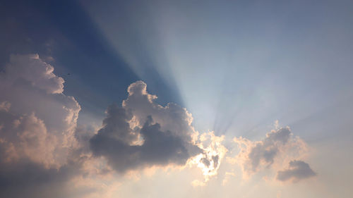 Low angle view of sunlight streaming through clouds