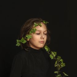 Portrait of young woman standing against black background