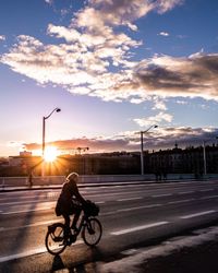 Man riding bicycle on road against sunset sky