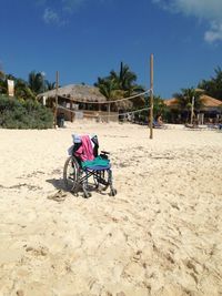 Wheelchair on sand at beach against sky during sunny day