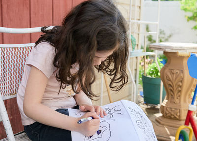 Young girl coloring pictures on a sunny day in the backyard