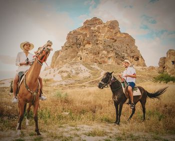 Full length of man and woman riding horses on field against mountain