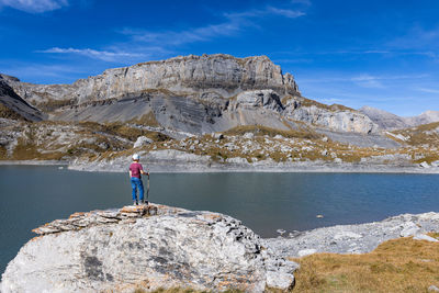 Rear view of woman standing on rock by lake against sky