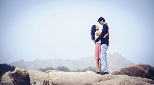 Man embracing woman while standing on rock against sky