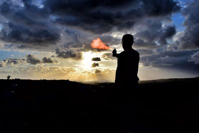 Silhouette man photographing against sky during sunset