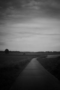 Empty road amidst field against sky