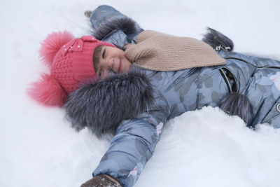 High angle view of smiling girl lying on snow covered land
