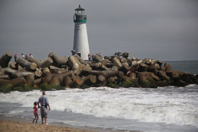 People on beach by sea against sky and lighthouse