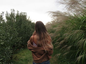 Rear view of woman standing amidst trees against sky