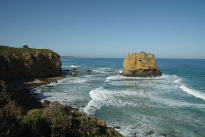 Scenic view of rocks in sea against clear blue sky