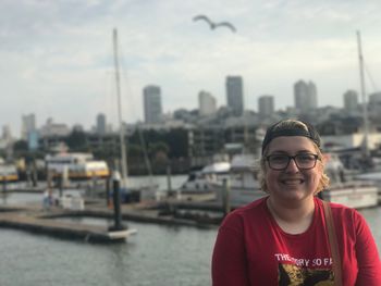 Portrait of smiling young woman by river in city against sky