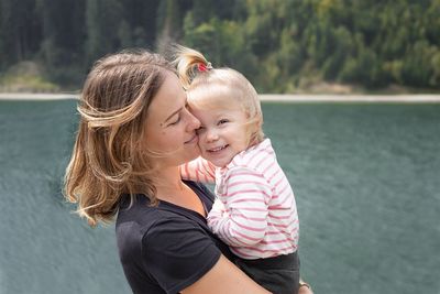 Mother carrying daughter by lake