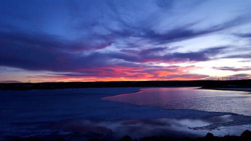 Scenic view of lake against dramatic sky during sunset