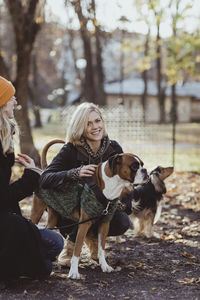 Portrait of smiling blond woman crouching by friend with dogs at park