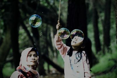 Mother and daughter looking at bubbles in forest